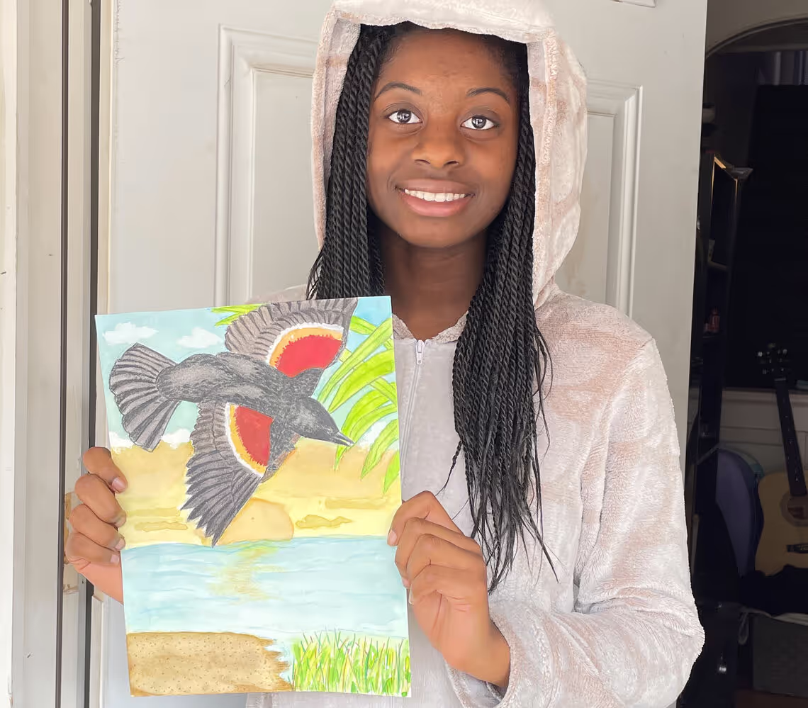 A woman holding up a painting of a bird